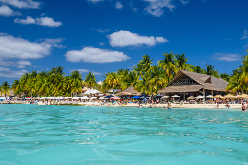 People sunbathing on the white sand beach with umbrellas, bungalow bar and cocos palms, turquoise caribbean sea, Isla Mujeres island, Caribbean Sea, Cancun, Yucatan, Mexico.