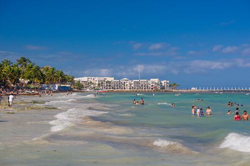 People swimming among splashes and waves on the beach with hotels in Cancun, Yukatan, Mexico.