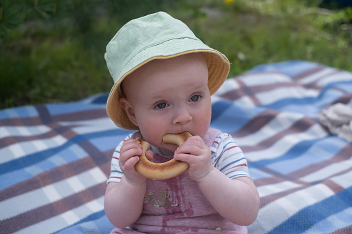 Portrait of cute baby with bread in her hands eating during picnic outdoor