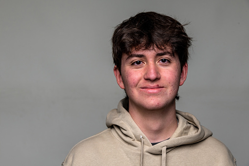 Smiling teenage boy front mugshot on gray background