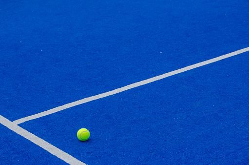 A ball on a blue paddle tennis court, racket sports