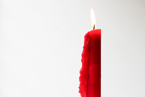 Front view of red color candle with flame with white color background.
