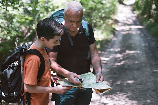 Happy grandfather and grandson looking at a map while hiking. Learning how to navigate with a compass. Getting away from it all.