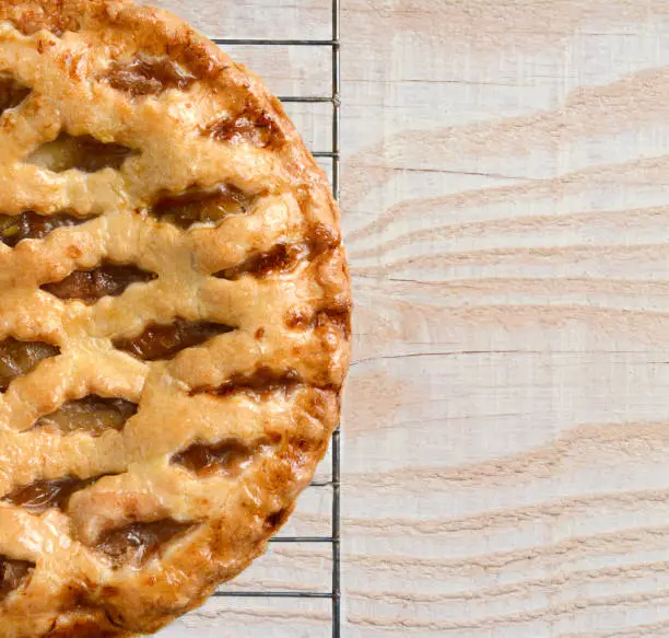 High angle view of a fresh baked holiday apple pie on a cooling rack atop a rustic wood kitchen table. Only half the pie is shown leaving copy space.