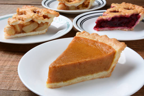 Pies Slices on Plates Closeup of four slices of pie on dessert plates. Focus is on the front slice of pumpkin pie. The back plates have apple and cherry pie. Horizontal format on an old wood kitchen table. sweet pie stock pictures, royalty-free photos & images