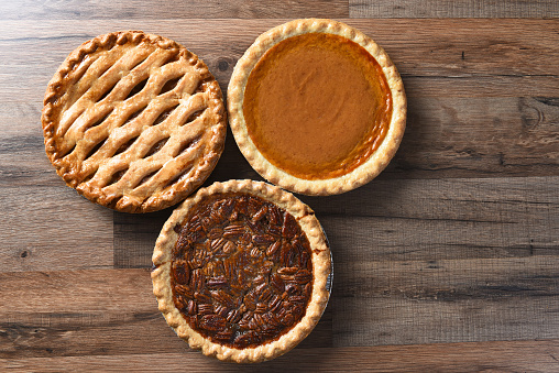 Three pies for Thanksgiving on a wood surface. The desserts include apple, pumpkin and pecan pies - all traditional treats for the American Holiday.