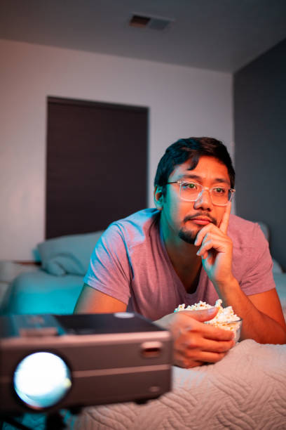 istock (Bored) Man Watching a Movie in Bed with Projector 1411510771