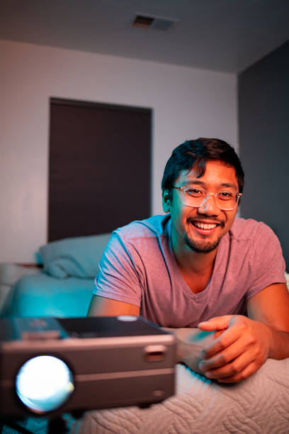 istock (Laughing) Man Watching a Movie in Bed with Projector 1411511718