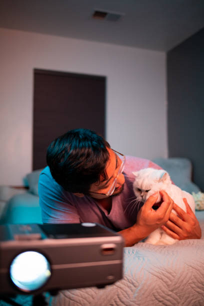 istock Man Watching a Movie in Bed with Projector with Cat 1411512849