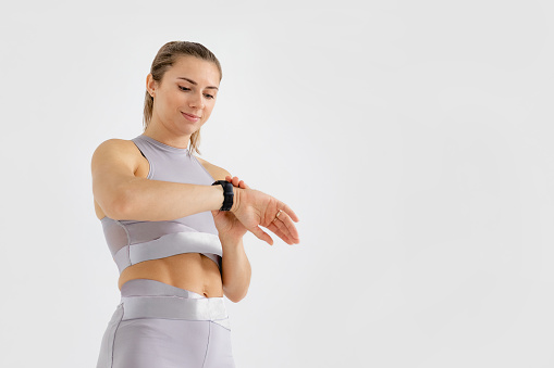 Portrait of sports woman at the studio. Caucasian girl on empty background. Fitness concept for exercise and muscular build. Professional athlete, girl power photography. Person is using gadget for training