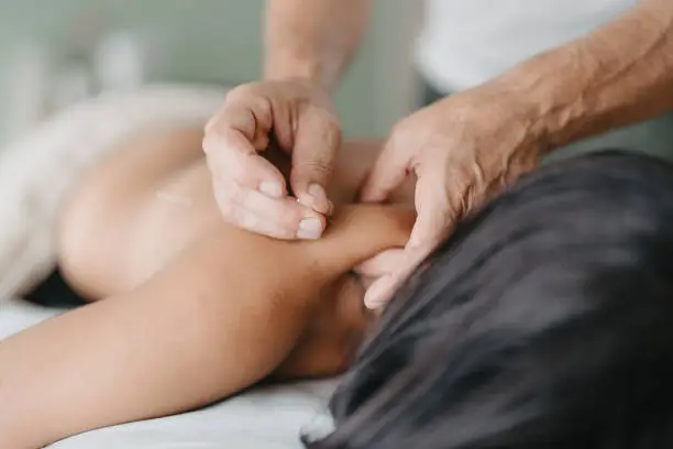 Acupuncturist pinches the patient's neck with one hand to insert an acupuncture needle with the other hand.