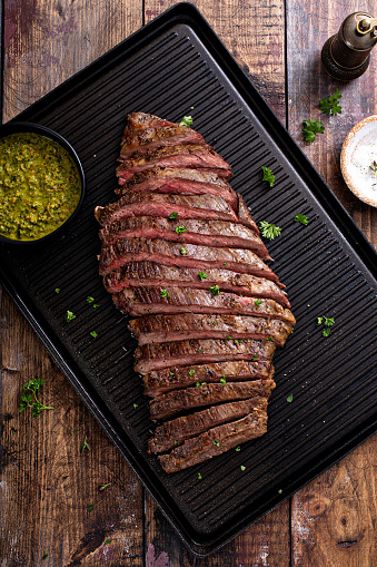 Grilled flank steak with chimichurri sauce on a grill pan on wooden table