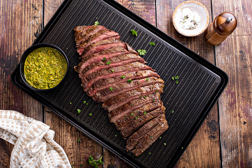 Grilled flank steak with chimichurri sauce on a grill pan on wooden table