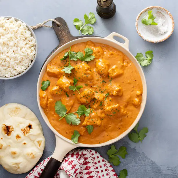 Chicken tikka masala, cooked marinated chicken chunks in spiced curry sauce, served with rice and naan bread top view in a skillet with copy space