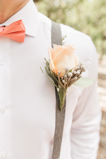 Groom's Pink Bow Tie & Rose Boutonnière on a White Button Down Dress Shirt Paired With Suspenders During a Wedding Ceremony Outdoors in July in Palm Beach, Florida.