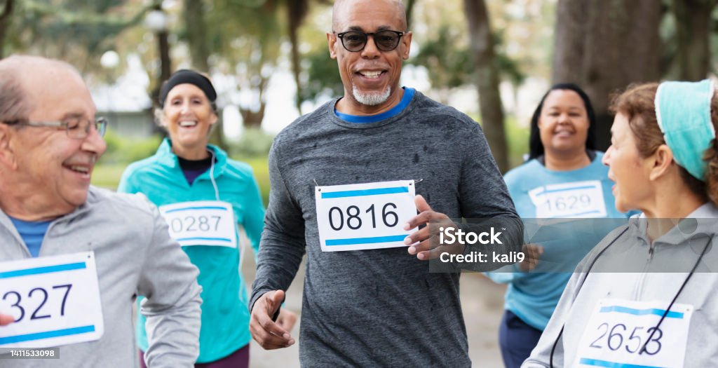 Senior African-American man running in a race A multiracial group of five men and women in their 50s and 60s running in a race at a park, wearing marathon bibs. The focus is on the African-American man, a senior in his 60s. Sports Race Stock Photo