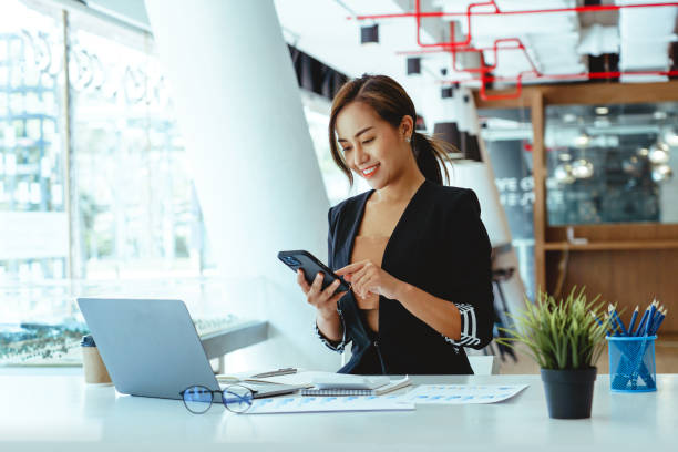 istock Modern workplace Asian business woman using mobile phone in office. 1411534017