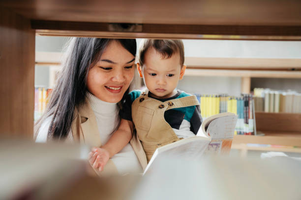 図書館で素敵な小さな息子に本を読んでいる若い母親 - bookstore student chinese ethnicity book ストックフォトと画像