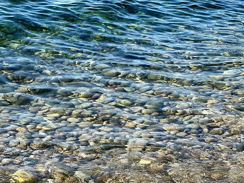 Pebbles under clear sea water waves. Smooth stones on the beach.
