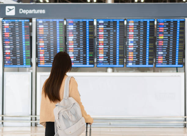 joven asiática en el aeropuerto internacional mirando el tablero de información de vuelo, revisando su vuelo. concepto de viaje. - airport business travel arrival departure board travel fotografías e imágenes de stock