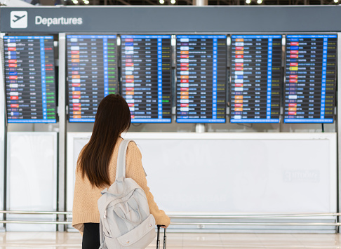 Young Asian woman in international airport looking at the flight information board, checking her flight. Traveling concept.