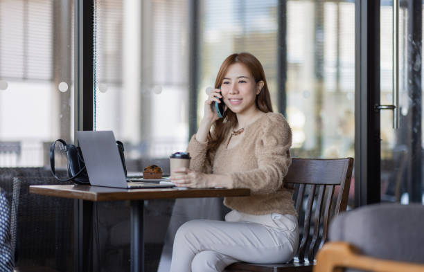 istock Asian businesswoman conversation on phone using a laptop while sitting in cafe 1411548556