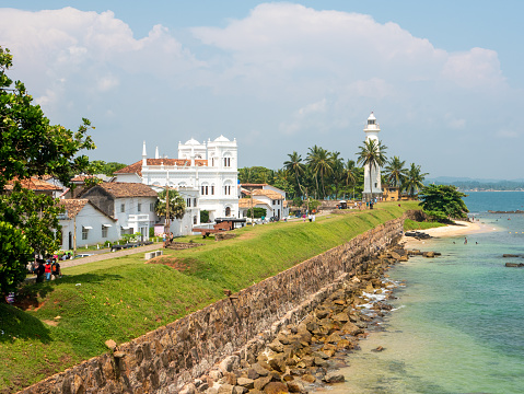 Galle, Sri Lanka - March 12, 2022: View of the white stone lighthouse and the fortress wall along the ocean in Galle Fort. Copy space.