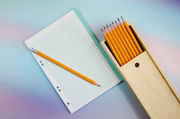 Photo of set of graphite pencils in wooden box and an empty blank. Pencils in pencil case and notebook sheet