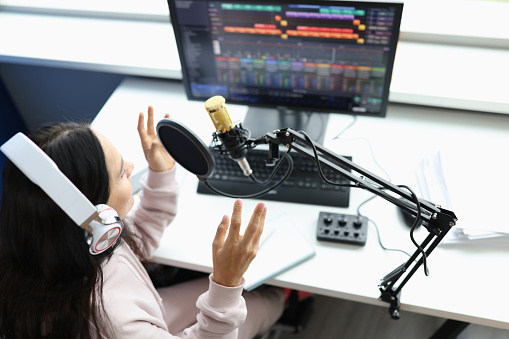 Woman in headphones in front of microphone broadcasts radio. Recording studio or streamer concept