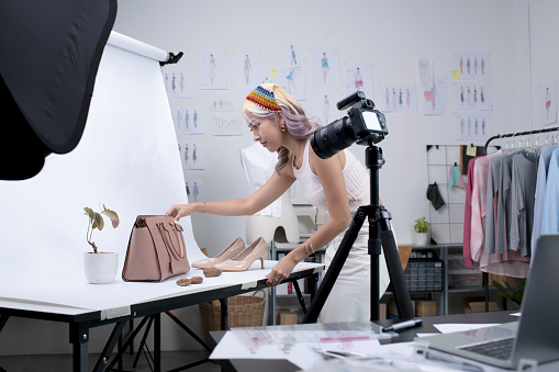 Asian woman fashion designer, influencer, blogger or vlogger preparing for fashion photoshoot and product live streaming using camera. Business online influencer on social media concept.