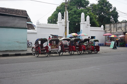 Surakarta,ID - July 16th, 2022. A row of becak or rickshaw parked on the road side of Pasar Klewer. Becak is a local rickshaw or pedicab tradional transportation from Indonesia.