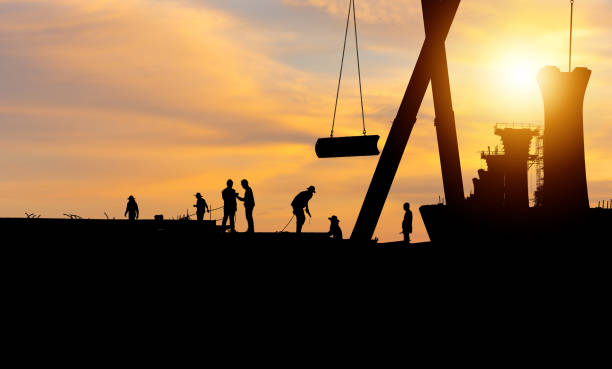 istock Silhouette of Engineer and worker checking project at building site background, construction site at sunset in evening time 1411556021