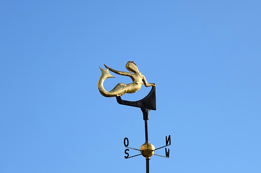 Gold colored weather vane in the shape of a mermaid. Blue sky in the background