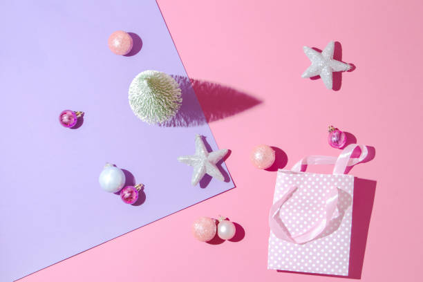 istock Minimalistic Christmas and New Year art composition. Miniature white spruce tree on pink and purple pastel background with Christmas balls and gift package. 1411560072