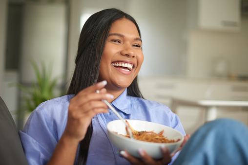 Young happy woman eating a healthy meal in the morning. Smiling and cheerful female enjoying a delicious bowl of cereal for energy and nutrition. One joyful lady having a plate of food for lunch