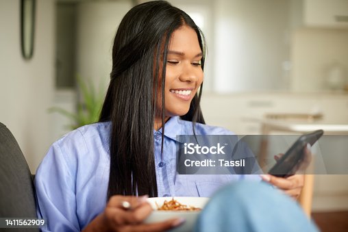 istock Young student sending a text message on her phone while eating breakfast. Beautiful culinary trainee looking for a new recipe online. One woman enjoying a meal alone at home while staying connected 1411562909