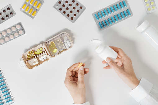 Pills box for daily intake of vitamins and medicines on white background. Top view glass of water and capsules and tablets in open plastic container in woman hands. Lifestyle for beauty and health