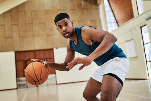 Young basketball player dribbling and bouncing a ball on a sports court during practice while training for a competitive match. Handsome baller exercising and working on his technique for match day