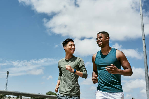 active men jogging outdoors on blue cloudy sky with copy space. two athletic guys or young sports friends running together, doing their routine cardio workout and fitness exercise in the city - adult jogging running motivation imagens e fotografias de stock