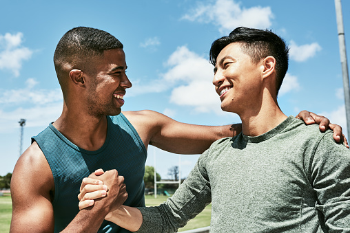 Male athletes giving a handshake and hugging in a friendly greeting on a sport field outside on a sunny day. Two young friends celebrating victory and embracing in joy after winning a race.