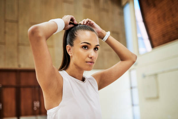 Fit young woman tying her hair while getting ready for exercising and training in a sport center or gym. One determined and dedicated athlete looking focused and prepared for a workout or competition stock photo