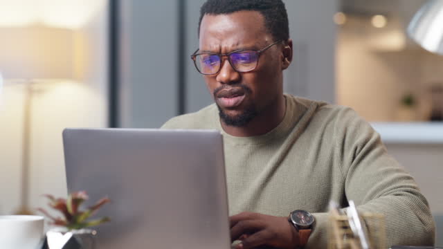 Stressed businessman looking unhappy and working on a laptop. Unhappy black man reading an email with bad news on a computer and working remote from home. Man dealing with debt or financial problems