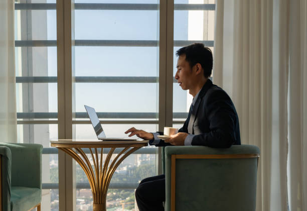 istock Male white collar sitting by the window and working with laptop 1411578964