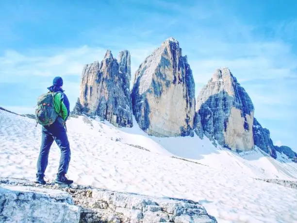 Photo of Backpacker On Trip Around Tre Cime Di Lavaredo In Sunny April Morning. View From Tour At Massive