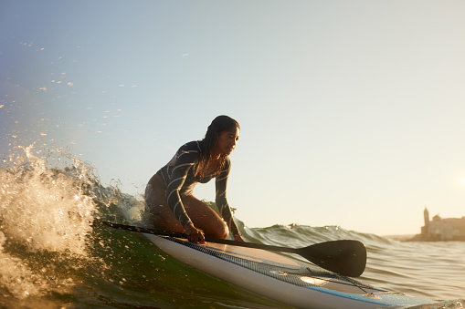 A Woman is on her knees on a paddle surfboard.