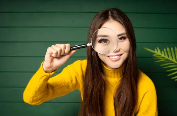 Photo of Curious brunette woman looking through the magnifying glass on a green wooden background.