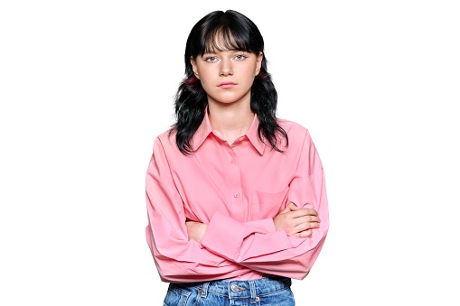 Sad young teenage female looking at the camera on a white isolated background. Confident girl student with arms crossed, emotions feelings seriousness concept