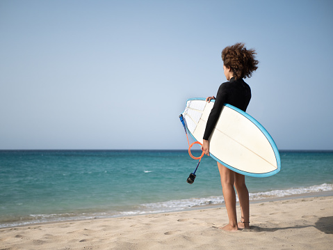 Young surfer woman from behind watching the waves on the beach shore