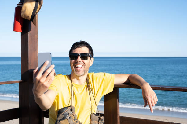 istock attractive Caucasian man enjoys his vacation during a summer oceanfront trip on the beach making a video call to his family and friends.concept travel and tourist destinations. 1411593866