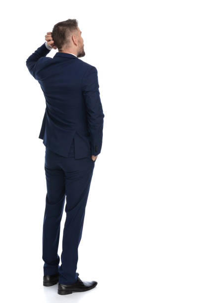 businessman scratching his head and pondering a decision rear view of a businessman scratching his head and pondering a decision, holding one hand in pocket worried man standing stock pictures, royalty-free photos & images